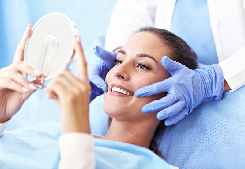 Smiling patient in Westlake, OH, holding a mirror after cosmetic dental treatment