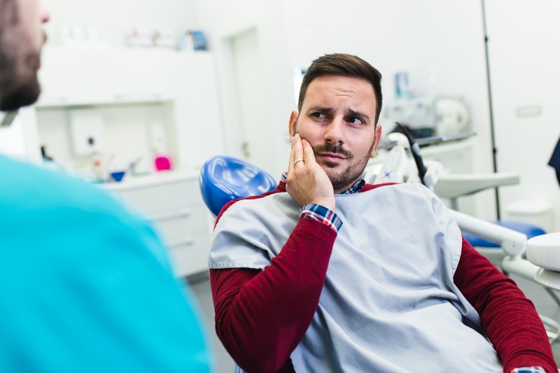 Patient holding jaw during dental exam for tooth sensitivity care in Westlake, OH